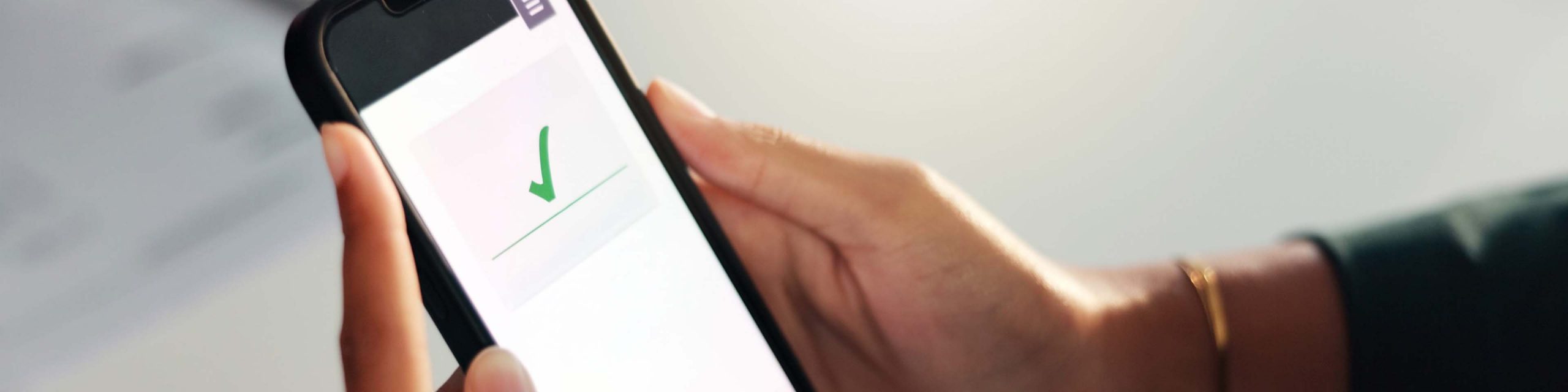 A person holds a mobile phone displaying a green tick on the screen.